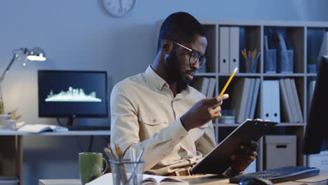 Handsome-Office-Worker-Manager-Sitting-At-Desk-While-Checking-In-The-Computer-Some-Data-In-The-Documents-In-The-Office-At-Night