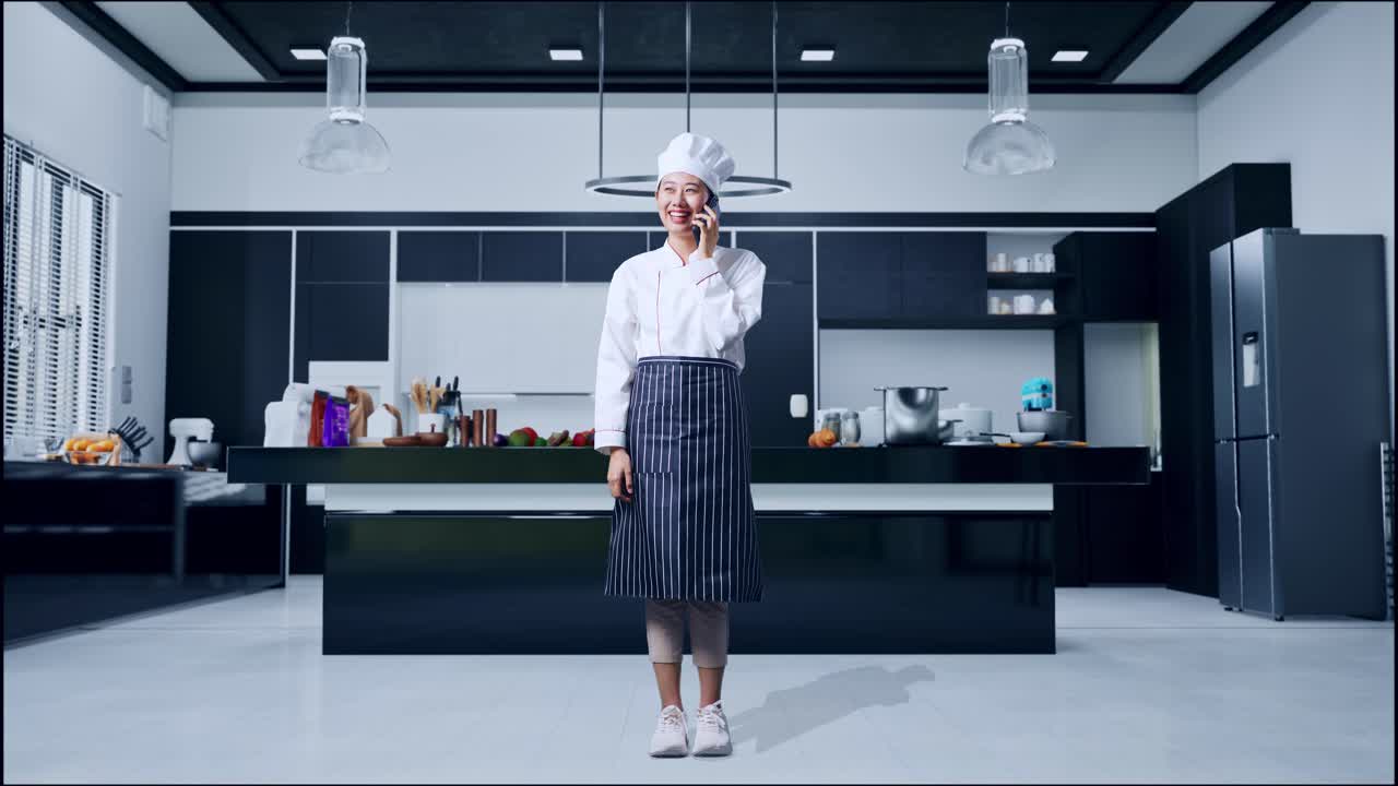 스마트폰으로 대화하고 집 주방을 둘러보는 아시아 여성 요리사의 몸이 가득 차 있습니다.