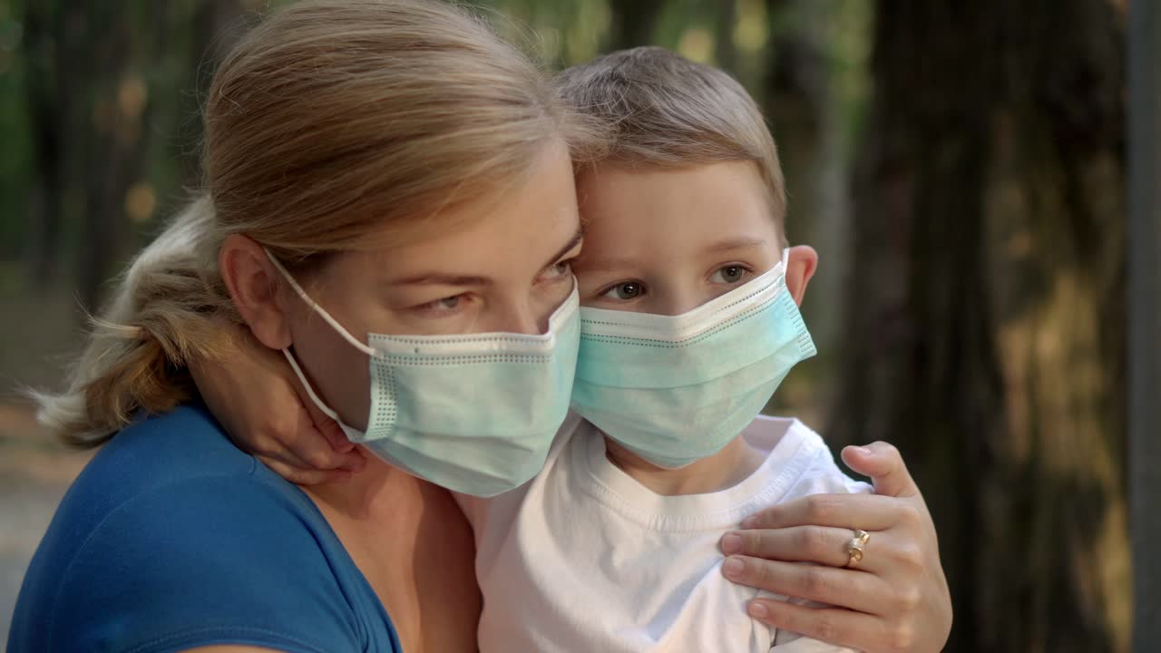 мать и сын в медицинских масках сидят в парке