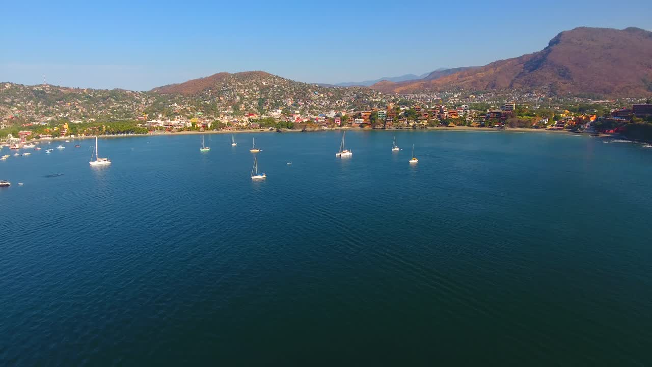 지후아타네호 근처의 산에 숨겨진 멕시코 도시 해안의 조용한 물의 만에 정박한 많은 항해 배의 공중 풍경