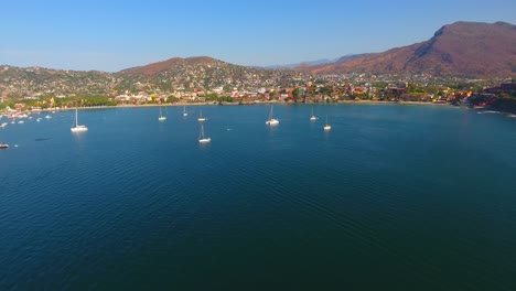 aerial view of many sailboats anchored in a calm water bay off the coast of a mexican city tucked into the mountains near zihuatanejo