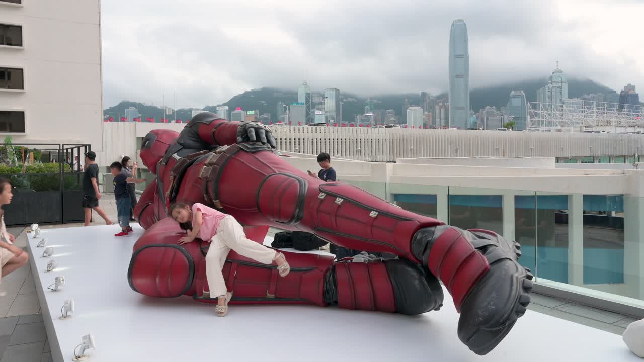 Kids scale an 8-meter Deadpool installation in Hong Kong, while tourists and locals snap photos. The display promotes Disney's new "Deadpool and Wolverine" movie.