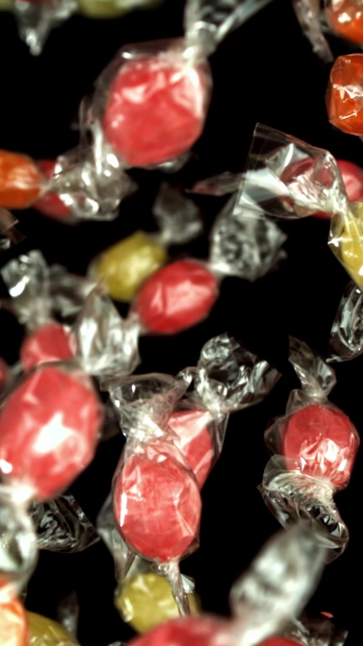 Caramelle incartate dai colori vivaci che cadono al rallentatore su sfondo nero