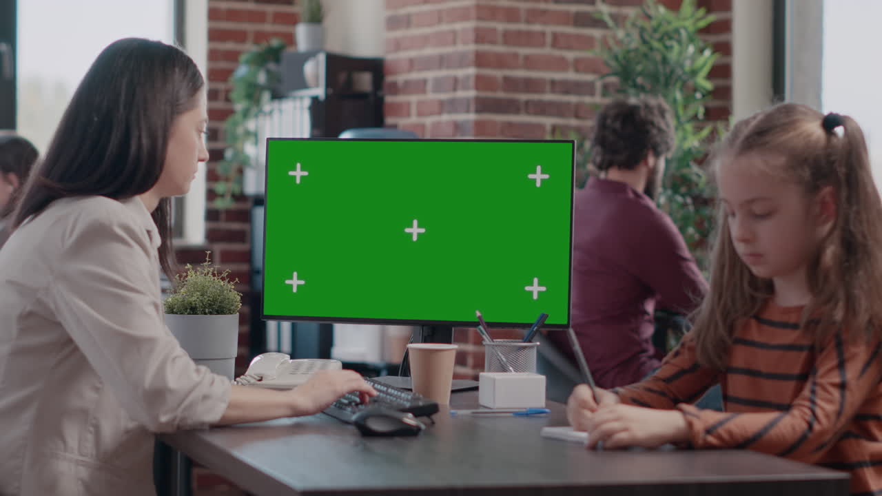 Single mom using computer with horizontal green screen, having little girl at office