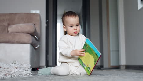 nice little kid sits on the floor with a book. adorable toddler tries to open the book but fails.