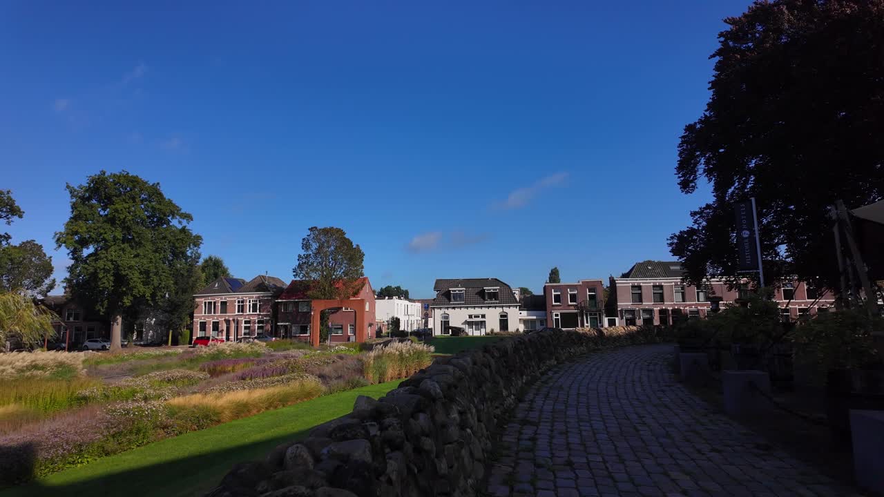 Traditional cobblestone walkway lined with houses, gardens and trees in Coevorden, Drenthe, Netherlands on a sunny day. (Coevorden, Drenthe, Nederland)