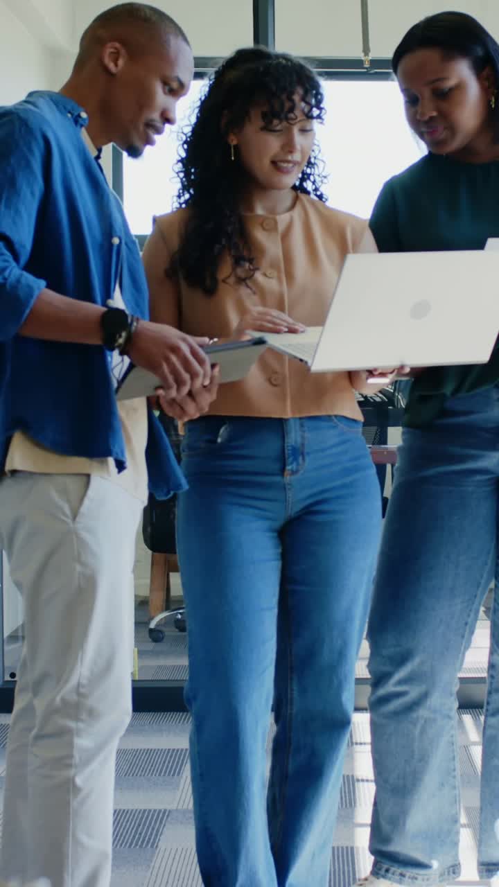 Vertical video: Reacting to laptop prompt, team pointing and typing in office with tablet and paper