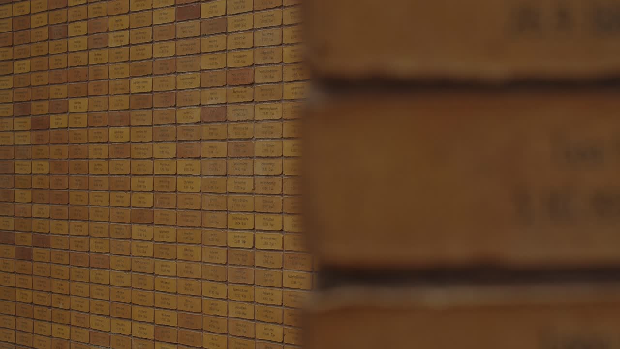 Focus rack from brick on wall of National Holocaust Names Memorial towards a large wall with bricks with the names of Holocaust victims.