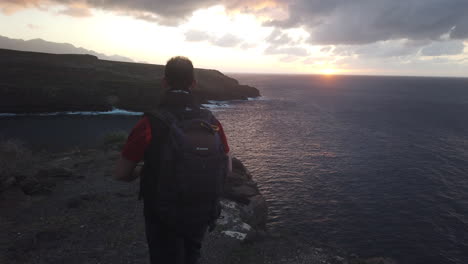 mature man with backpack on his back walks along the cliffs of the coast of the municipality of galdar during sunset