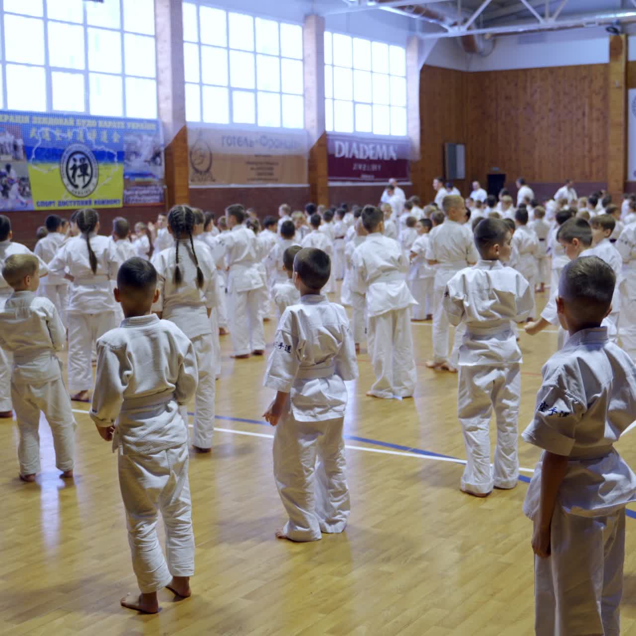 Spacious gym crowded with numerous young sportsmen standing in rows. Teenage karate trainees applauding to coaches