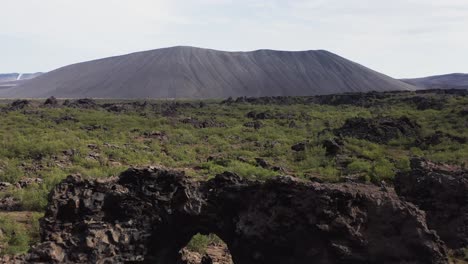 Adventure-couple-stands-in-solid-lava-tube-at-Dimmuborgir-field,-aerial