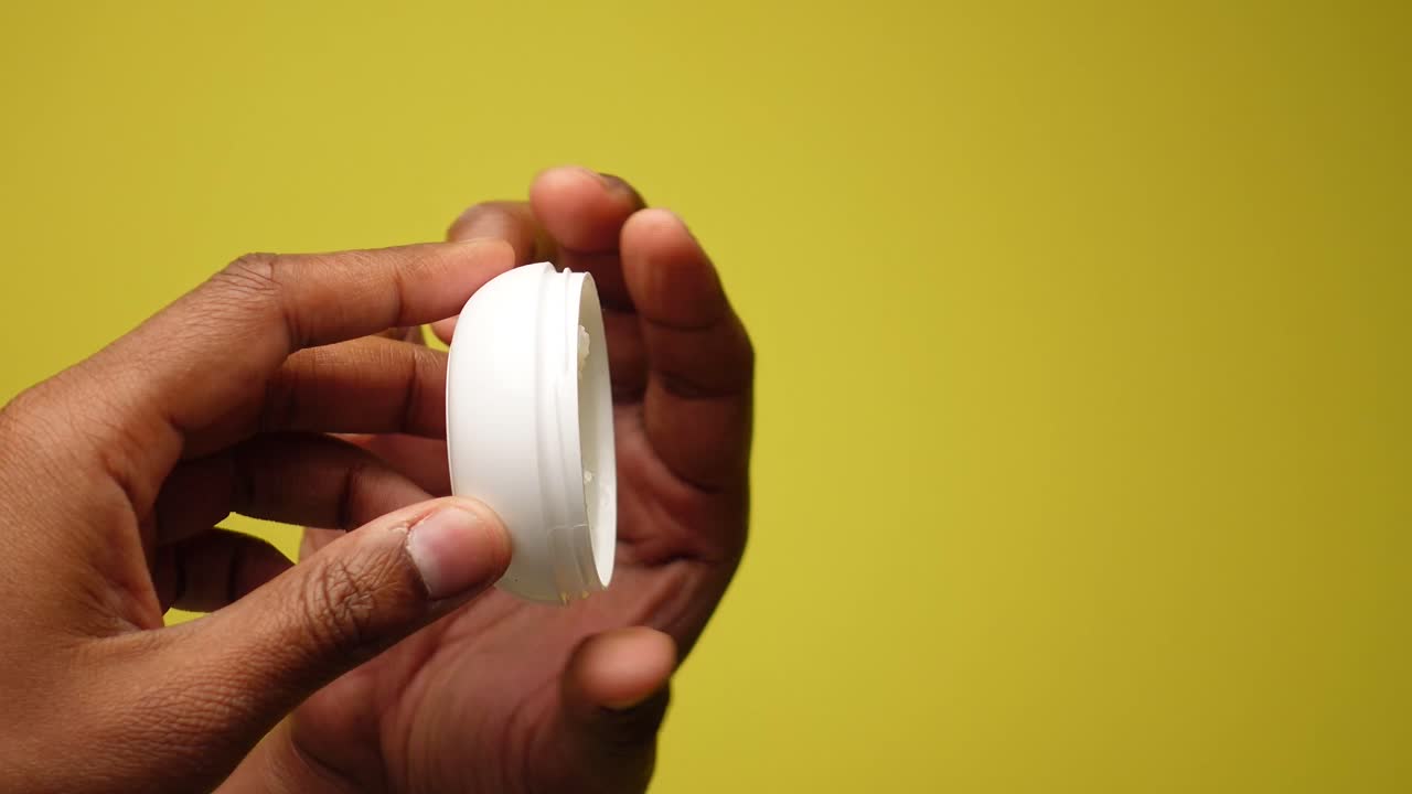 Opening a white plastic container of cream or balm