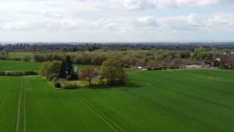 Rural-British-farmhouse-establishing-aerial-view-with-lush-green-trees-and-agricultural-farmland-countryside-fields