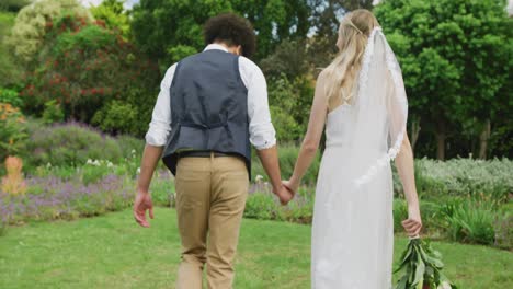 happy diverse couple walking in garden on sunny day at wedding