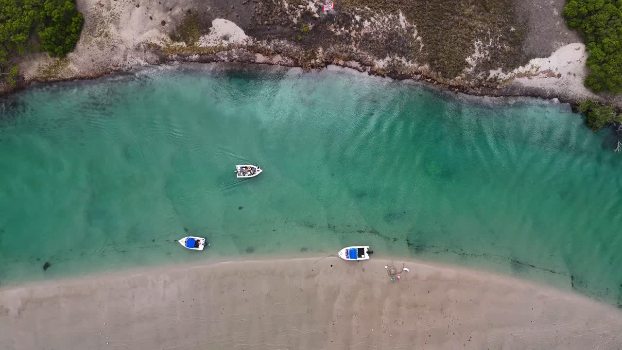 Aerial top down ascend of boats in Swansea swimming area with people in clear green water near road