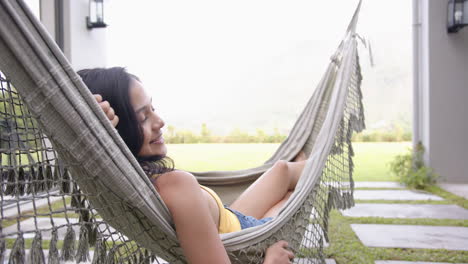 a young biracial woman relaxes in hammock, smiling contentedly, copy space