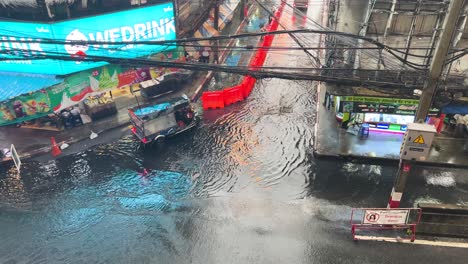 tuk-tuks and motorbikes drive through a heavily flooded urban road in bangkok, thailand, under overcast daylight with visible reflections and slow-moving traffic