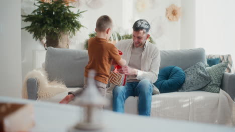 young boy helps dad tie bow on christmas present