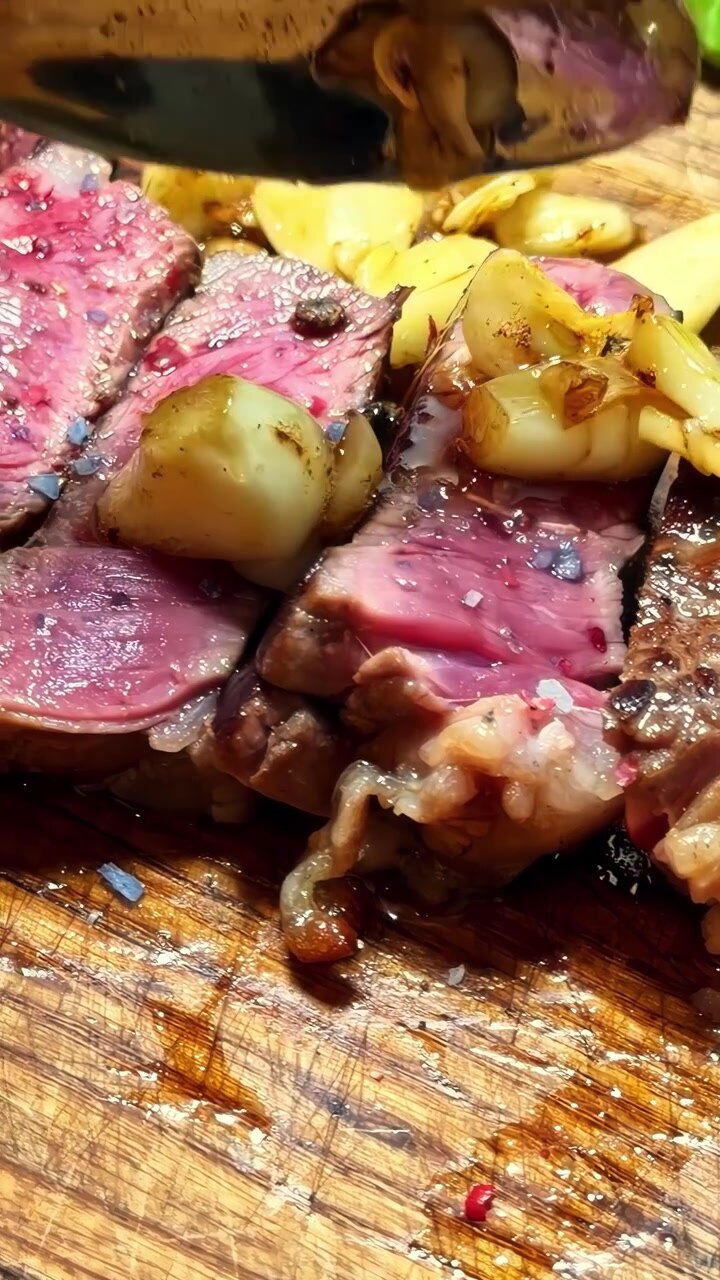 Steak setengah matang yang diiris dengan taburan bawang putih panggang di samping tunas asparagus segar. Sempurna untuk presentasi kuliner atau tutorial memasak.