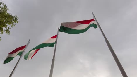 tres banderas húngaras en astas de bandera que soplan en el viento con nubes de tormenta en el fondo - cámara lenta de 120 fps