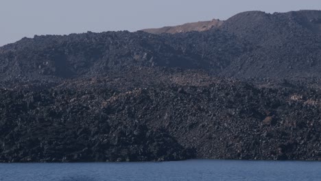 paisaje volcánico en fira, santorini con terreno rocoso y aguas azules tranquilas