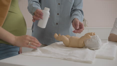 maestra y estudiante poniendo talco para bebés en un bebé de juguete