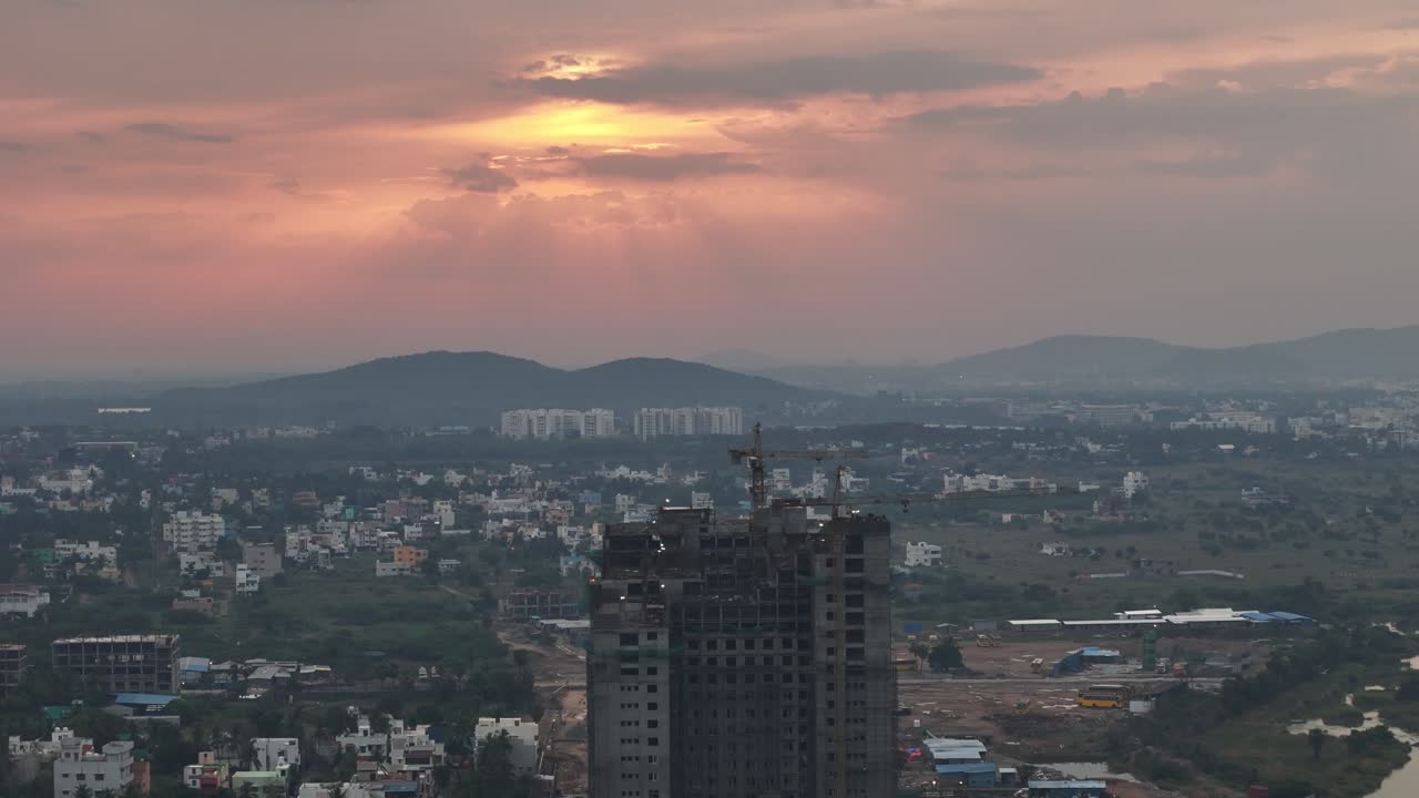 Drone footage at golden hour showcases the contrast between new urban development and nature. A large, built high-rise dominates the , situated between finished apartments and a calm body of water