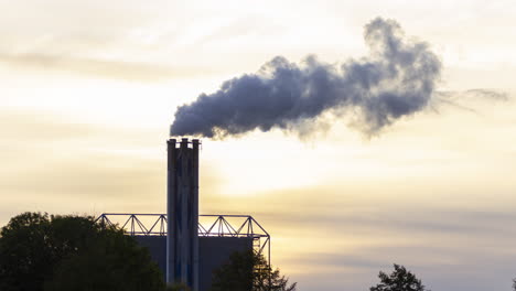 Time-lapse-of-smoking-factory-chimney-against-the-background-of-a-setting-sun---slow-zoom-out