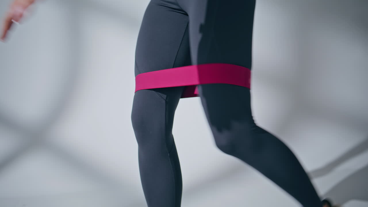 Sportswoman legs squats workout with rubber resistance band at empty wall space