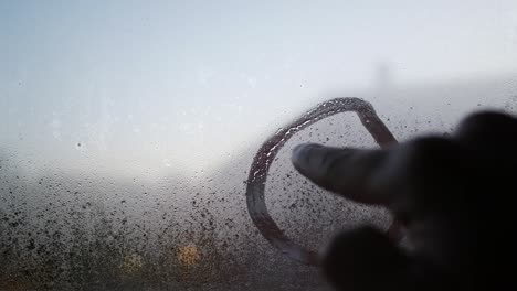 hand drawing sad face on foggy window glass with condensation