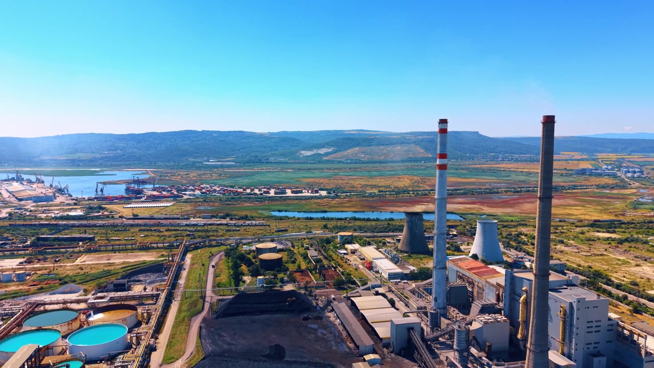 Power plant near the river and land area. A view of a power plant with tall chimneys next to a river and open land. The scene shows industry and nature together.
