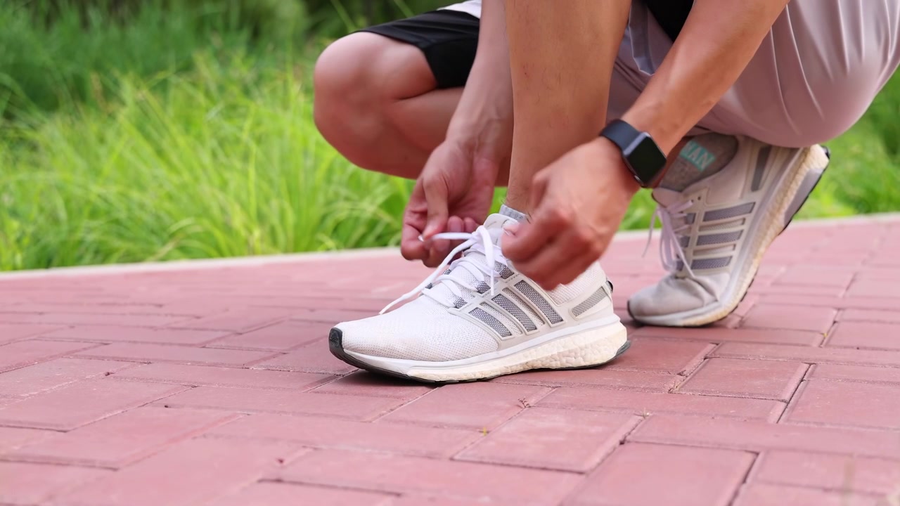 Mani di un uomo che allaccia la scarpa da corsa, legando i lacci, pronto per l'allenamento di jogging all'aperto nel parco. L'immagine cattura la preparazione e la determinazione per una sessione di fitness all'aperto.