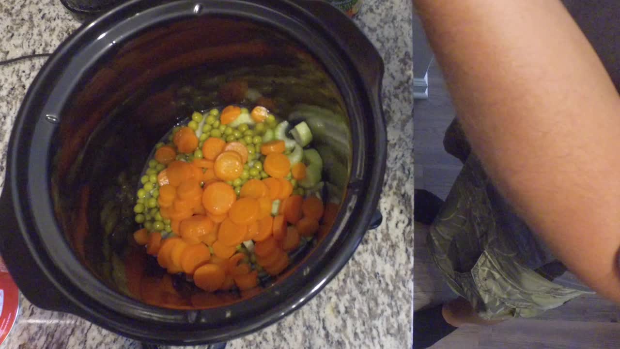 cocinar un guiso en una olla de cocción lenta mirando hacia abajo en la olla y revolviendo los guisantes, zanahorias y otros ingredientes