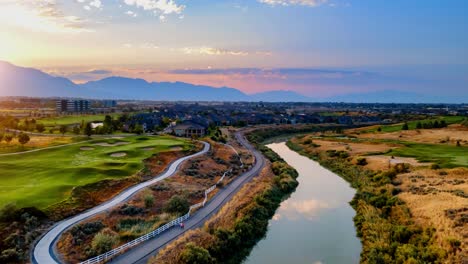 aerial hyperlapse over a river with the rising sun and an idyllic community with a golf course, commuter train and a city in the valley