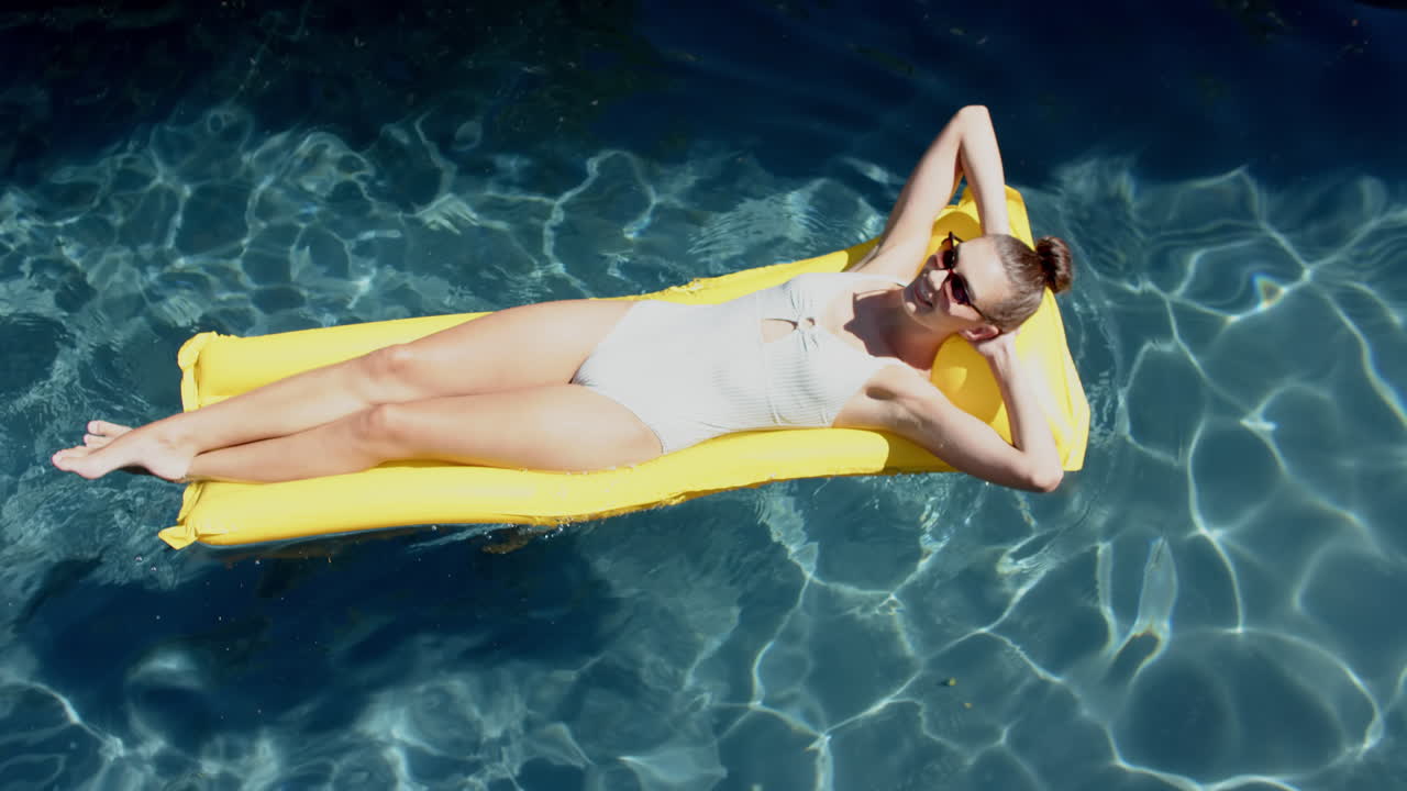 Teenage Caucasian girl relaxes on a yellow pool float, wearing a white swimsuit