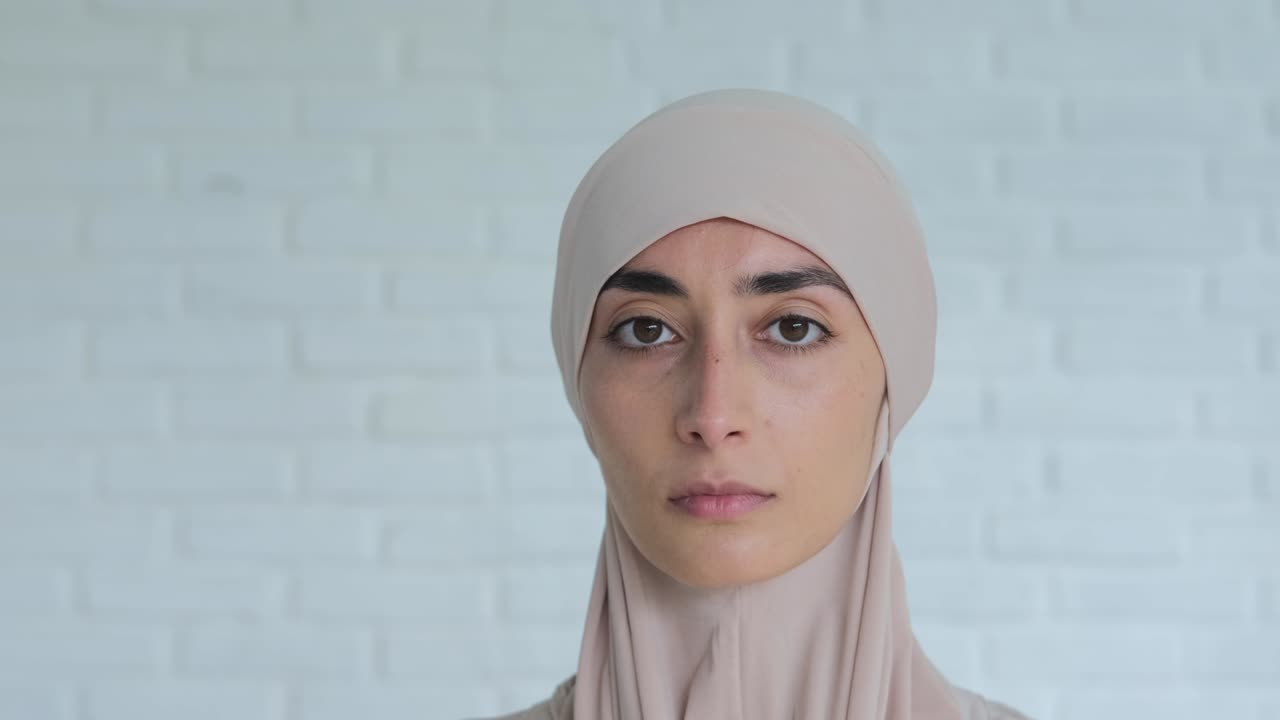 색 배경에 히자브를 입은 멋진 이슬람 여성에 대한 평온하고 슬픈 감정 표정. 슬픈 표정은 겸손하게 카메라를 바라보고, 여성은 이슬람의 규칙을 준수합니다.