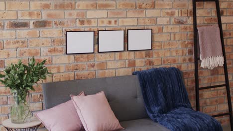 Three-wooden-frames,-plant-and-sofa-with-copy-space-on-brick-wall