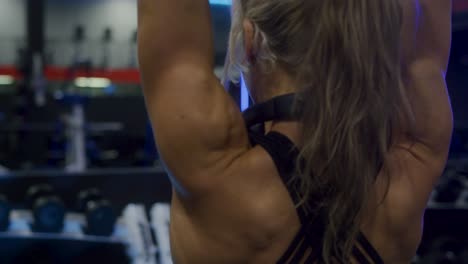 slow motion shot of a fit girls back while she works out doing tricep extensions over head in front of the mirror
