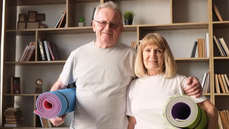 elderly couple holding yoga mats at home