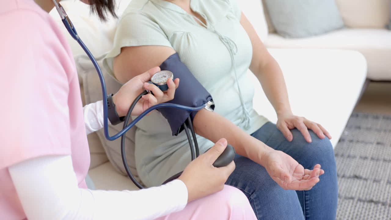 Measuring blood pressure, nurse assisting senior asian woman during home visit