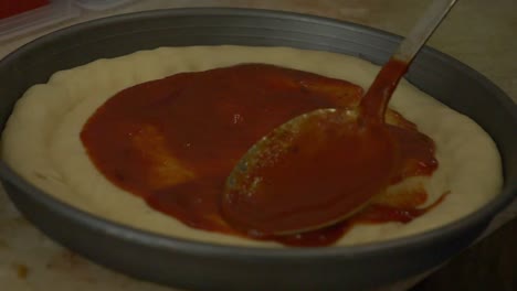 tomato sauce being spread on pizza dough by metal spoon