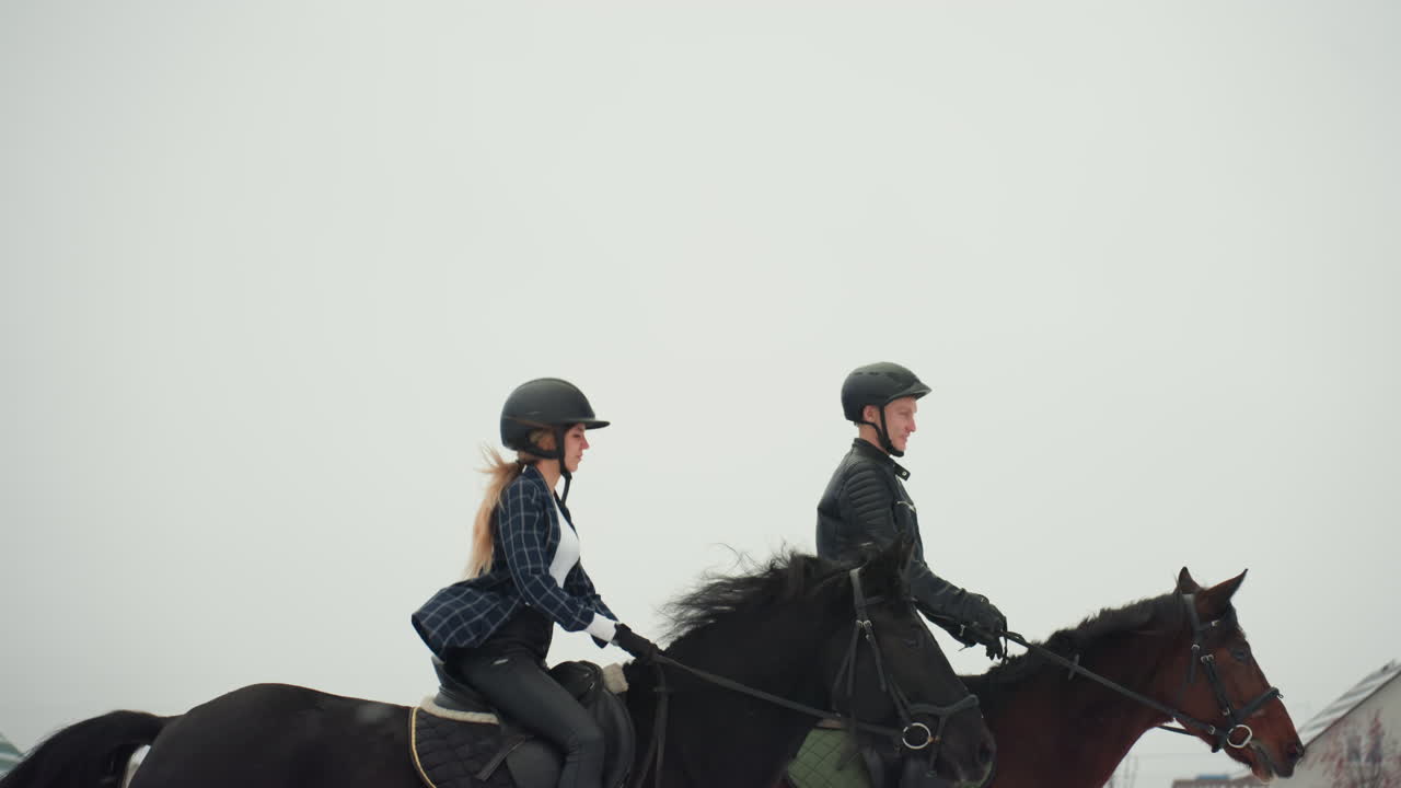 Lezione di equitazione in tandem su un campo nuvoloso che mostra due cavalieri con i caschi che guidano i cavalli a passo costante, dinamica istruttore-allievo, focus su postura, sella e redini, atmosfera invernale calma