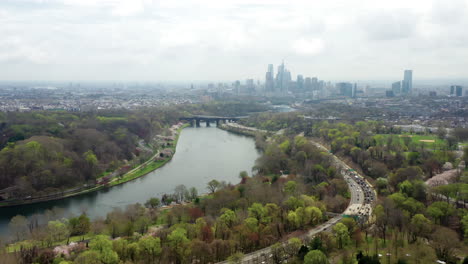 aerial drone pan left of philadelphia city skyline from above the schuylkill river and highway traffic showcasing spring trees and cherry blossoms