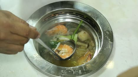 delicious hot pot soup in a stainless bowl with shrimp, vegetables, and corn - closeup shot