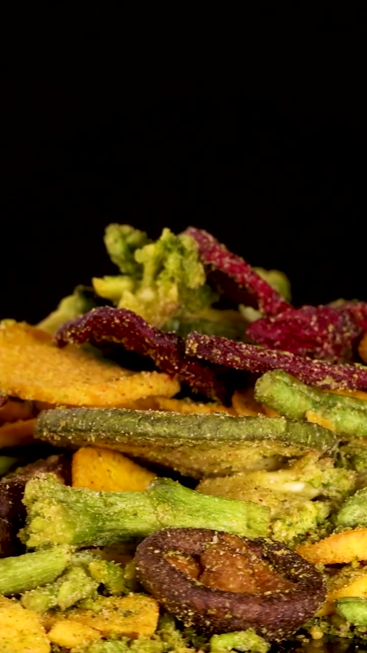 Un vivace assortimento di chips di verdure essiccate ruota in un primo piano verticale su sfondo nero