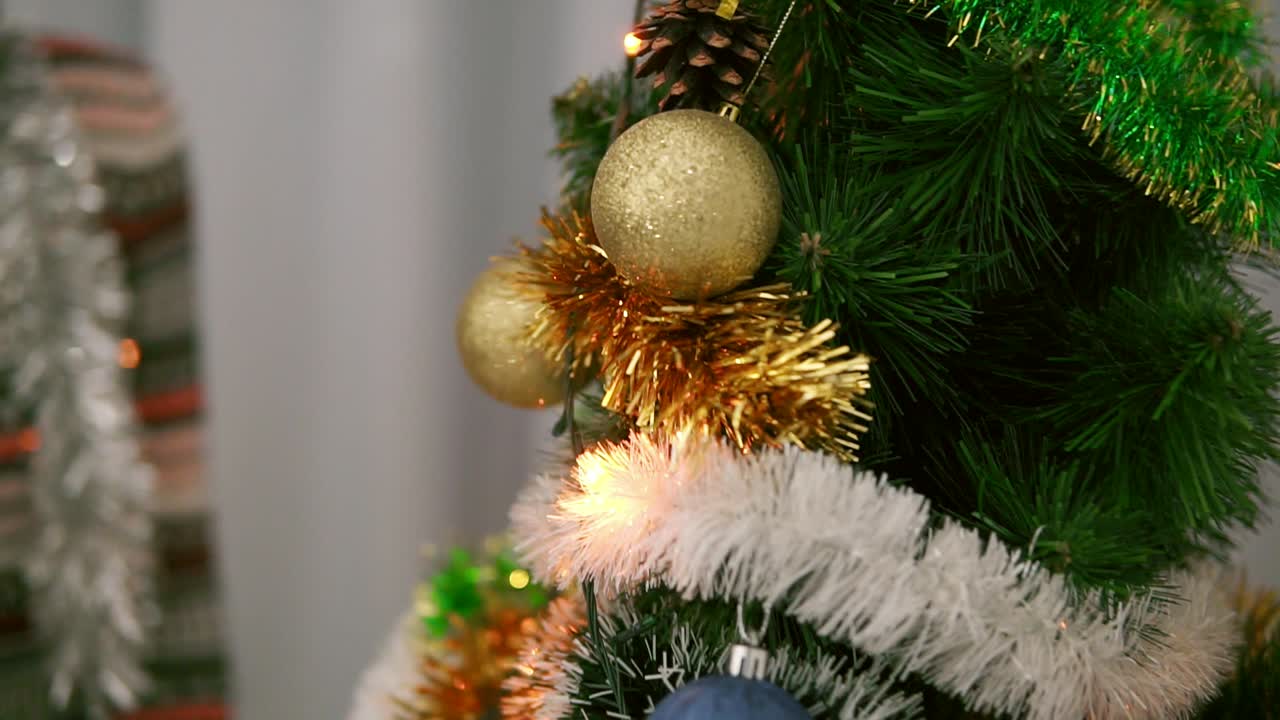 atractiva mujer feliz con suéter navideño sonriendo y decorando un árbol de navidad con juguetes en su apartamento. tiro en cámara lenta