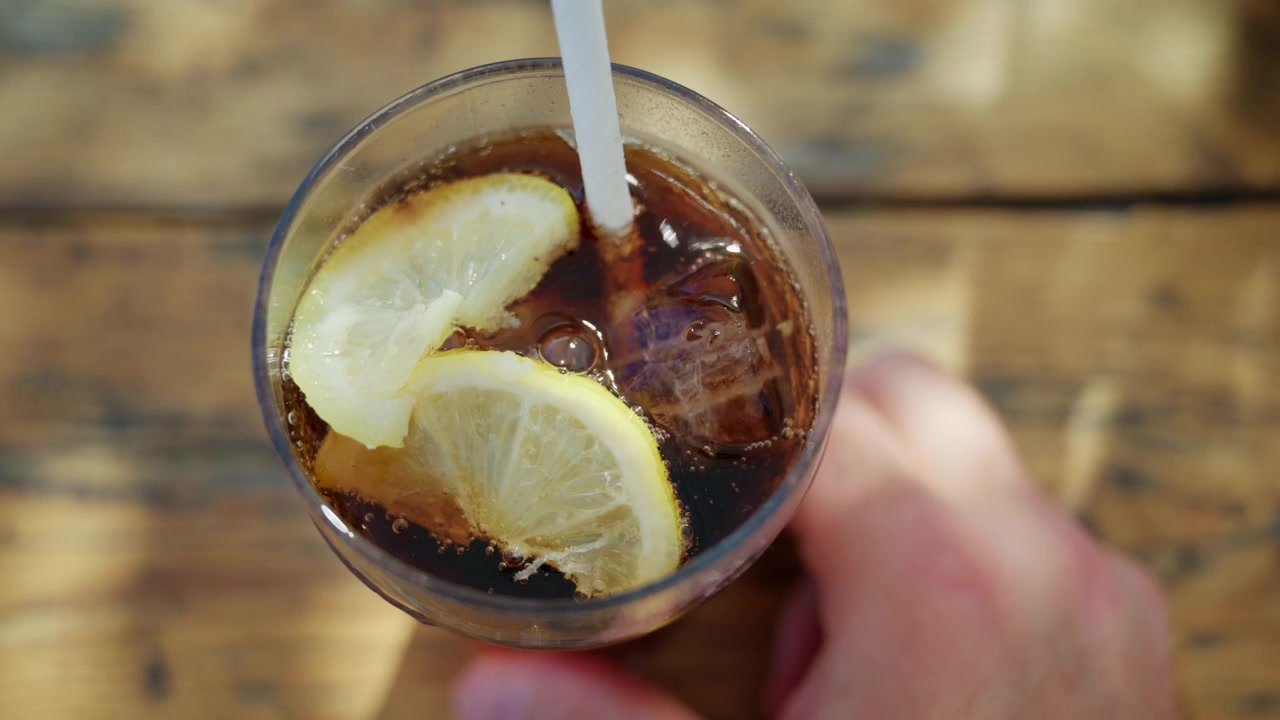 Primo piano di una cola ghiacciata con fette di limone e bollicine in un bicchiere trasparente.