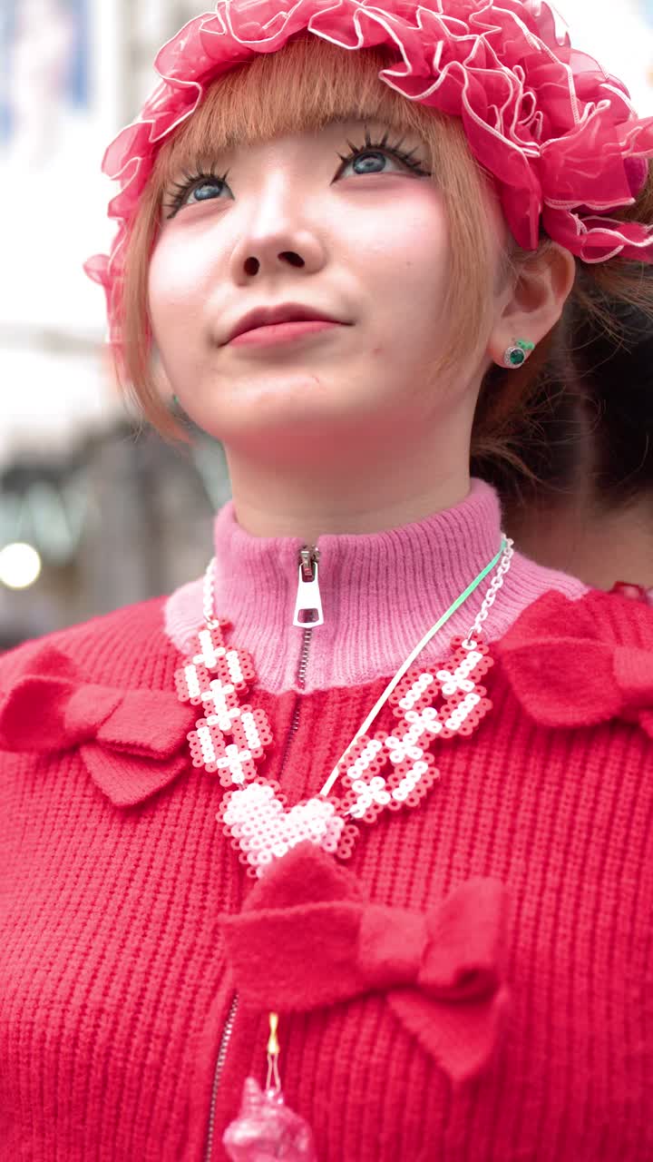 Due donne che indossano abiti vivaci in stile decora rosa stanno insieme nell'affollato incrocio di Shibuya