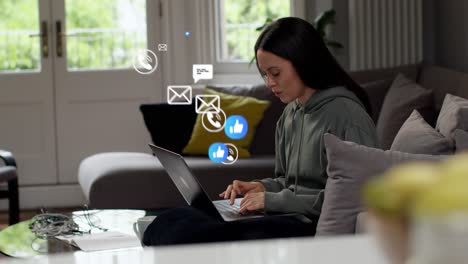 mujer sentada en el sofá trabajando desde casa en una computadora portátil con emojis de gráficos de movimiento que muestran múltiples notificaciones de mensajería y redes sociales