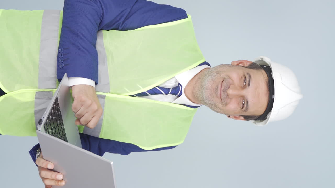video vertical del ingeniero sosteniendo una computadora portátil riéndose de la cámara.